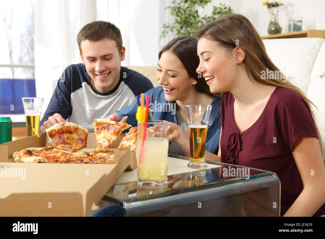 Tre amici a parlare e mangiare la pizza seduti sul pavimento del salotto di casa Foto Stock