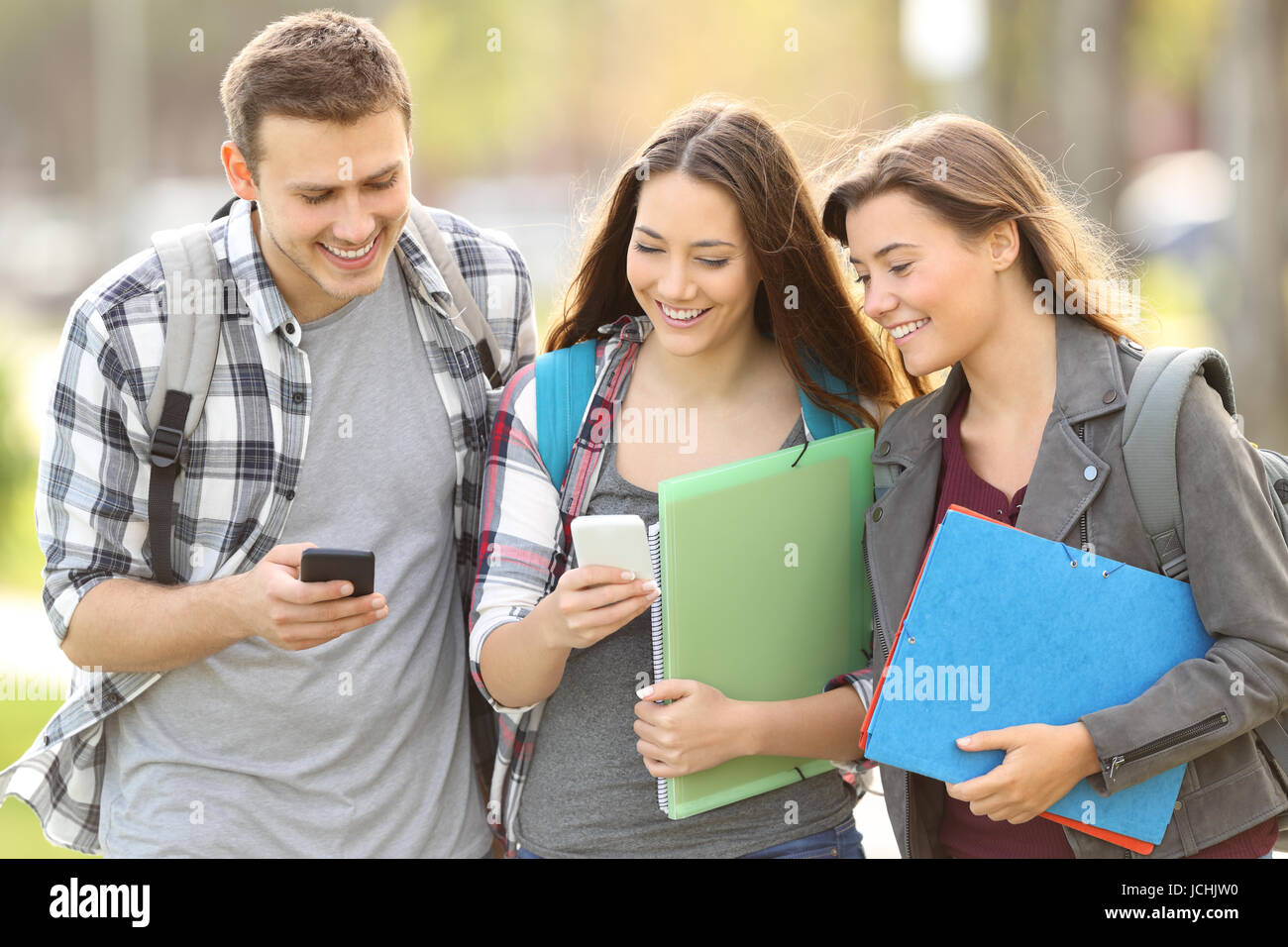 Tre Allievi felici controllo smart phone all'aperto in un campus universitario Foto Stock