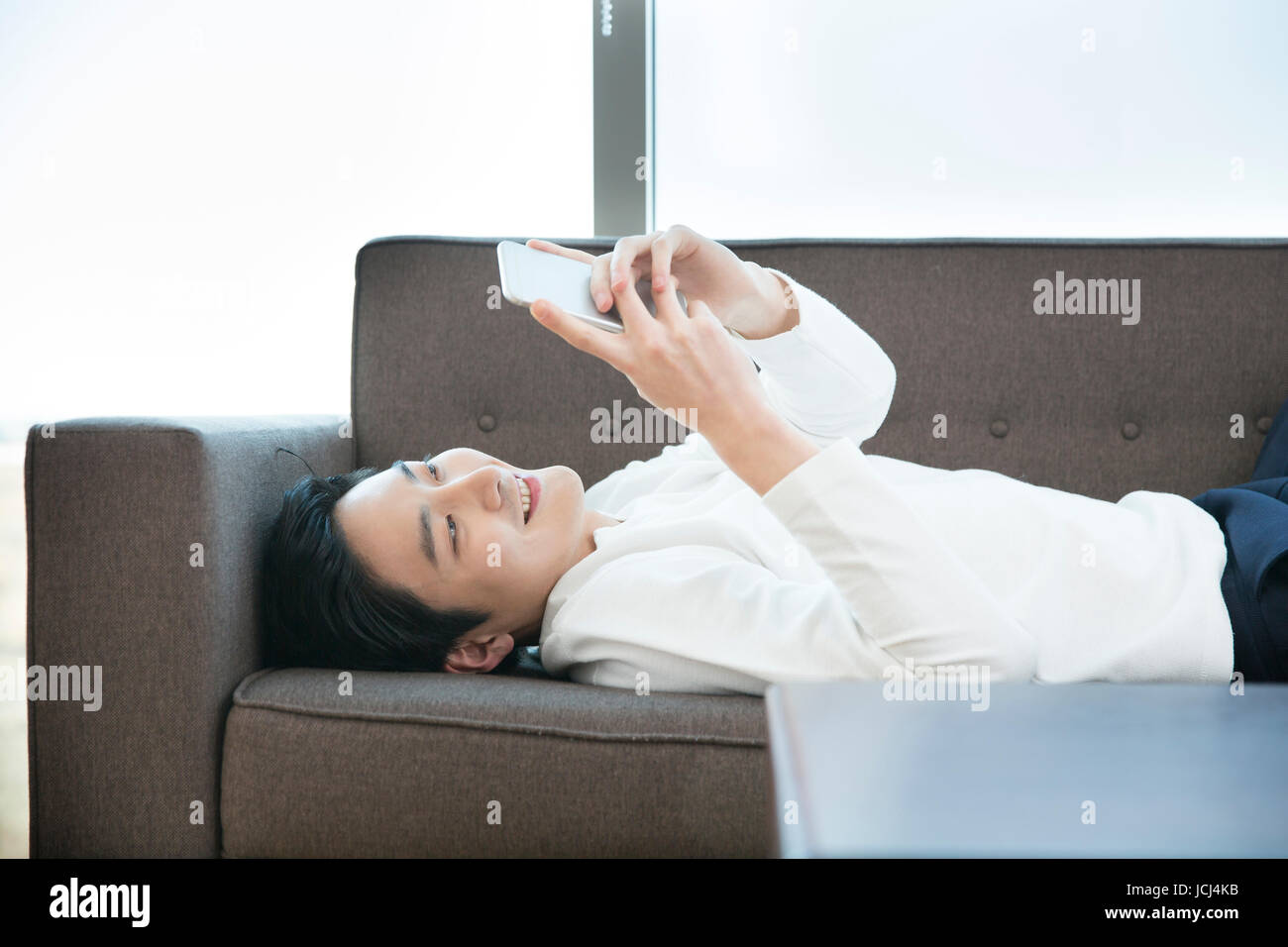 Giovani sorridente bachelor utilizza lo smartphone rilassante sul divano Foto Stock