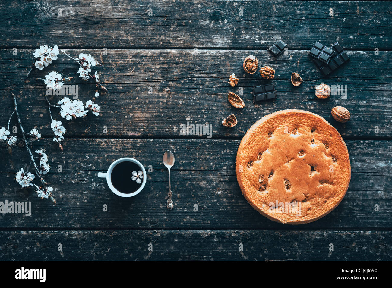 La tazza di caffè e torte fatte in casa con noci e cioccolato su una vecchia tavola di legno e rami fioriti di pesco in primavera. Foto Stock