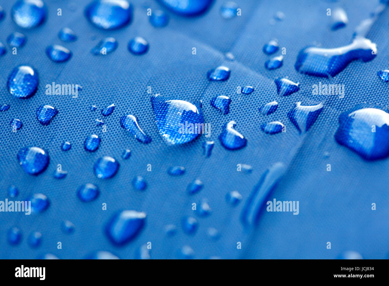 Primo piano di gocce di pioggia su un ombrello blu Foto Stock