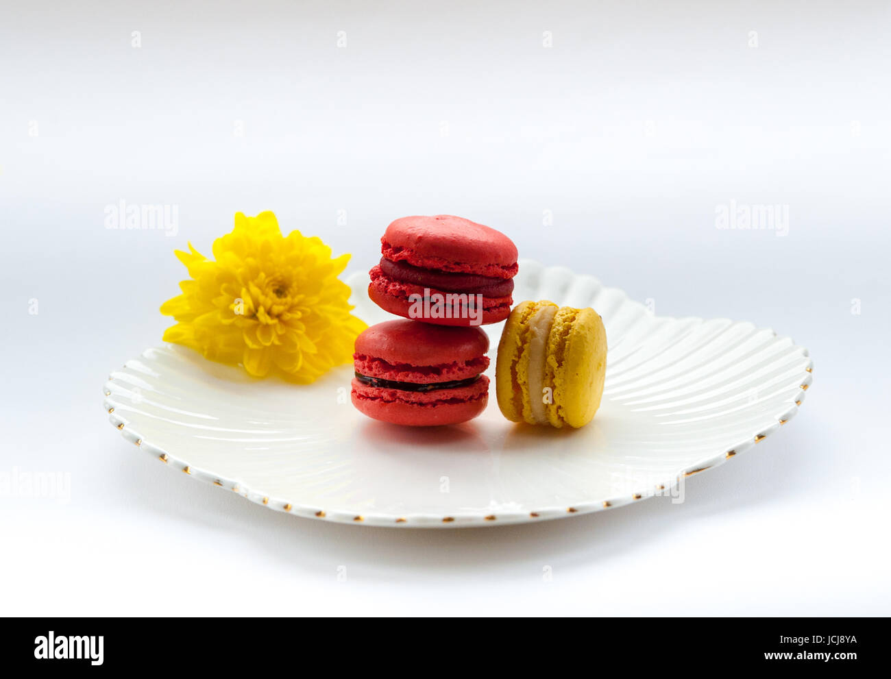 Macaron colorati su un vintage piastra bianca con un fiore giallo Foto Stock