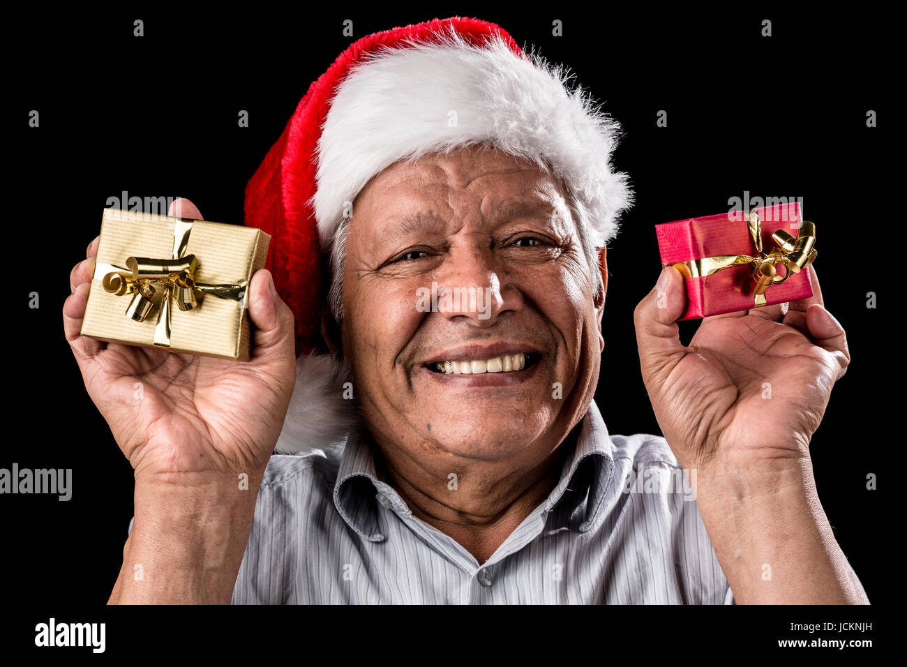 Venerati uomo brimming sopra con un sorriso. Egli indossa un Kris Kringle hat. Tenendo in mano un piccolo dono avvolto in ogni mano, oro e rosso. Tema Natale. Sfondo nero. La messa a fuoco sugli occhi. Ampio DOF. Foto Stock