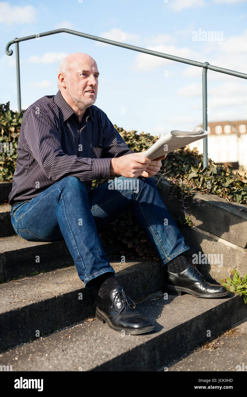 Mann mittleren altera, Senior sitz mit einer Zeitung auf einer Treppe im Frühling im Freien Foto Stock