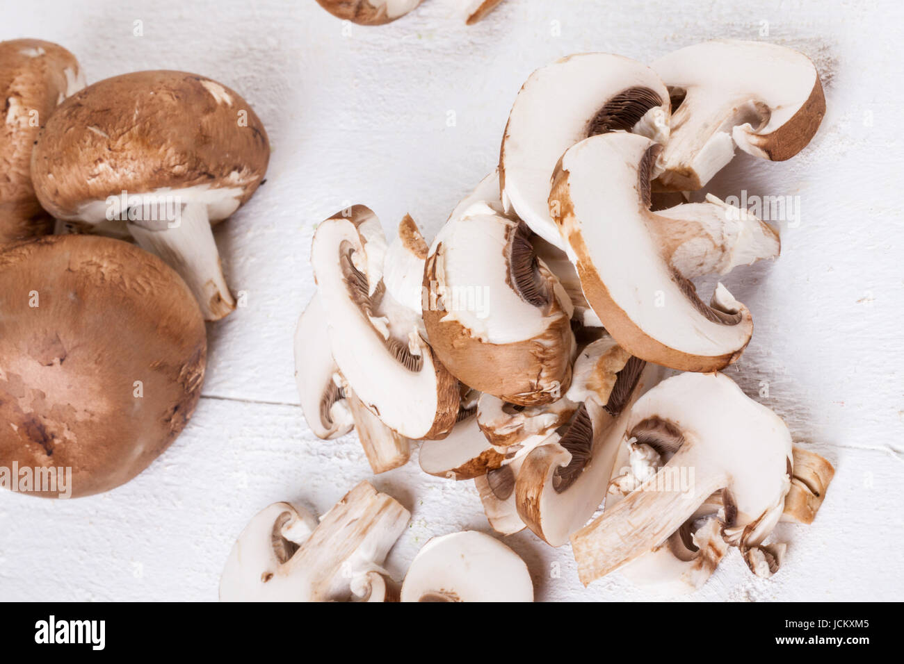 Frische Steinchampignons Champiggnons im ganzen und in Scheiben geschnitten auf einem weißen Holzbrett Foto Stock