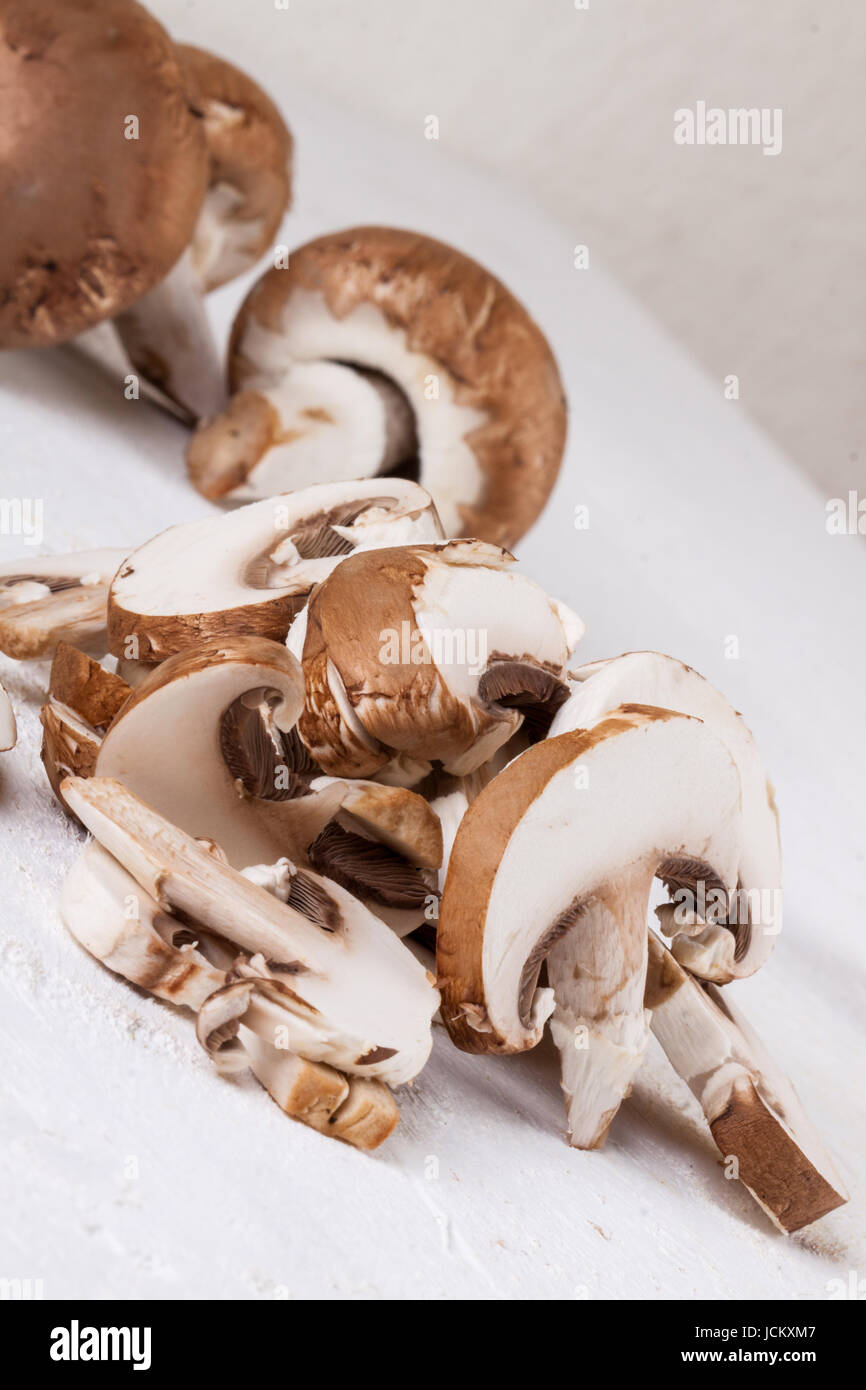 Frische Steinchampignons Champiggnons im ganzen und in Scheiben geschnitten auf einem weißen Holzbrett Foto Stock