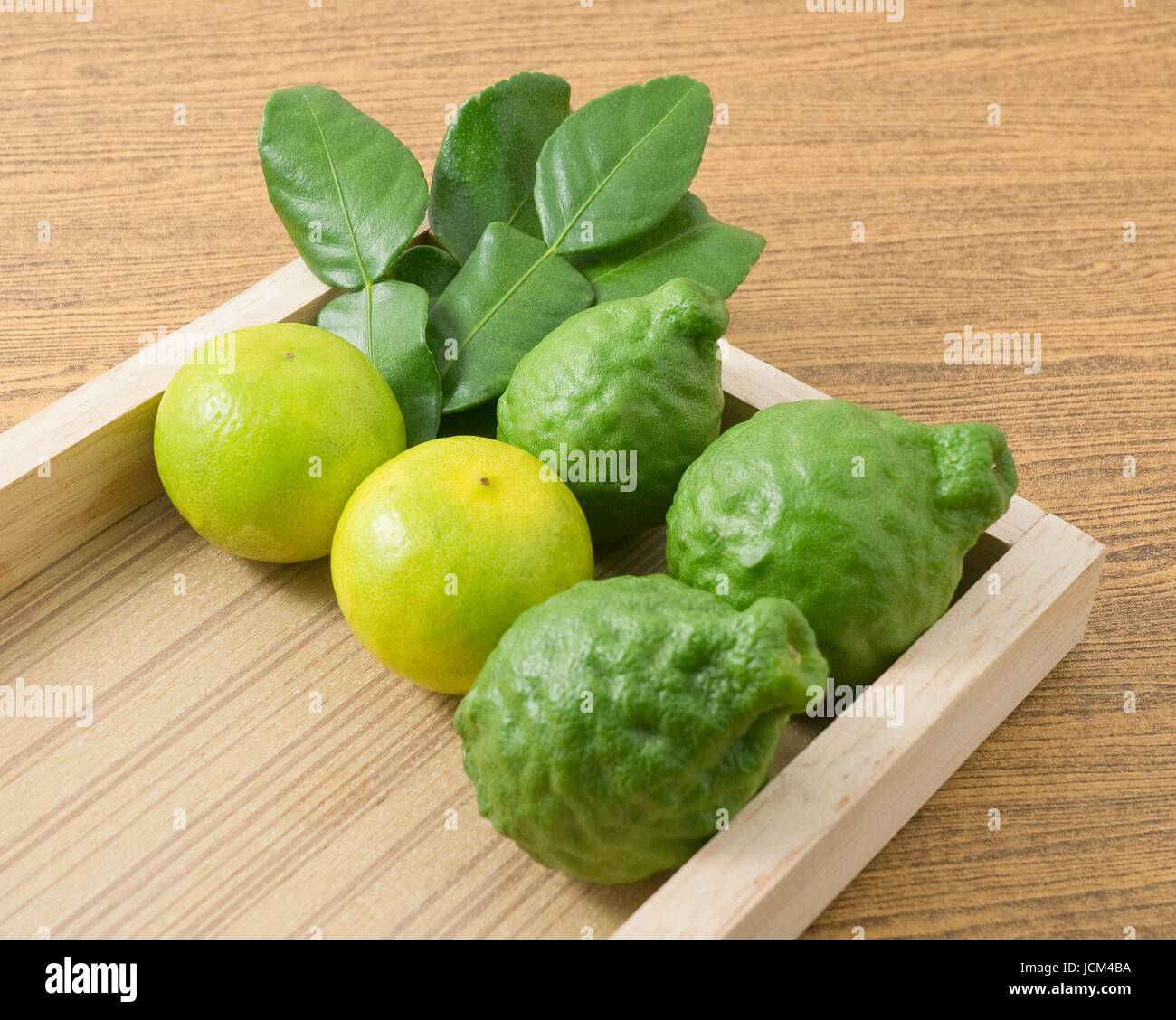 Vegetali e le erbe, Combava persiano con lime e foglie di Kaffir per condimento in cucina su un vassoio di legno. Foto Stock