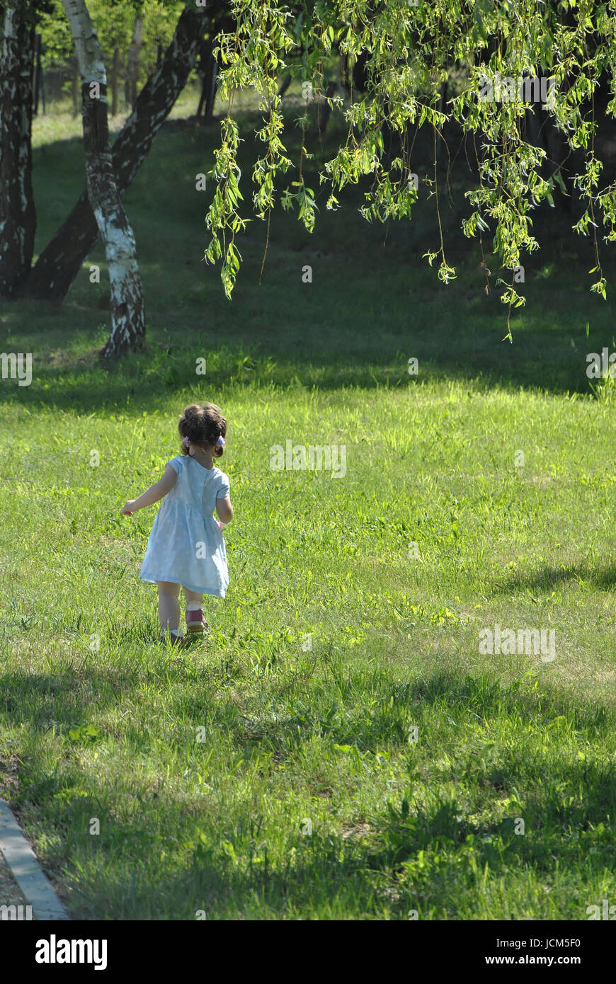 Una bambina cammina con cautela sull'erba tra gli alberi Foto Stock