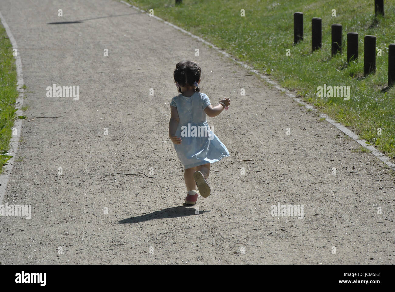 Una bambina di due anni di corse in un vestito blu su una strada di ghiaia Foto Stock