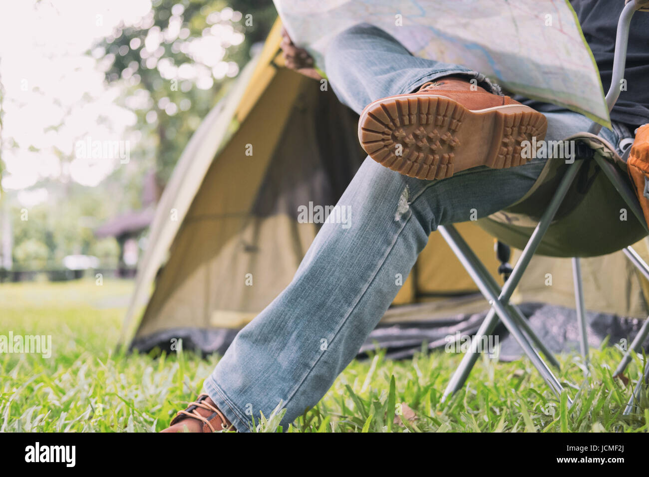 Turista uomo seduto su una sedia e la lettura mappa nella parte anteriore della tenda al campeggio nella foresta. Attività all'aperto in estate. Viaggi avventura in nazionale p Foto Stock