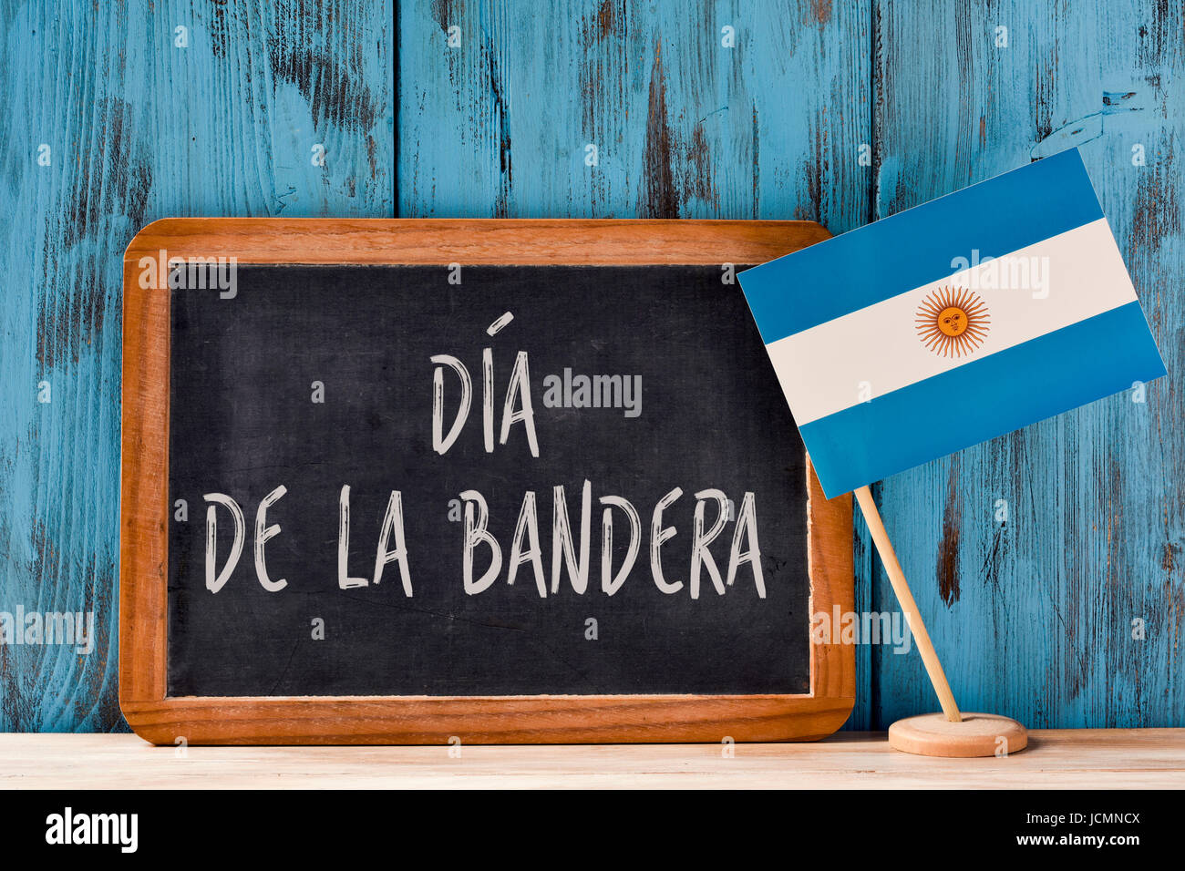 Il testo Dia de la Bandera, Giornata di bandiera scritto in spagnolo in una lavagna e una bandiera dell'Argentina, su un rustico di una superficie di legno, contro un legno blu ba Foto Stock