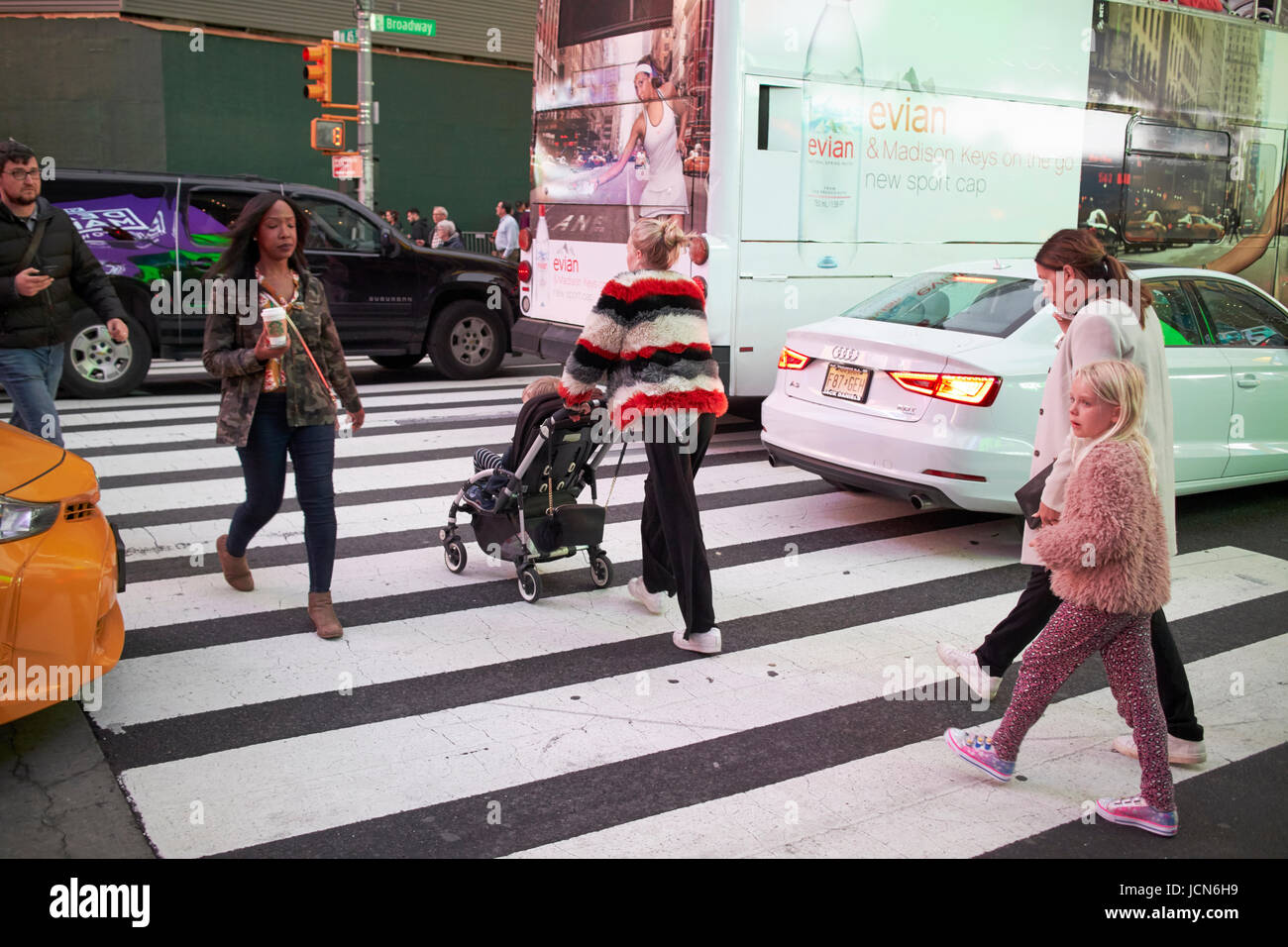 Donna spingendo bambino nel passeggino attraverso crosswalk nella trafficata e traffico di sera in Times Square a New York City USA Foto Stock