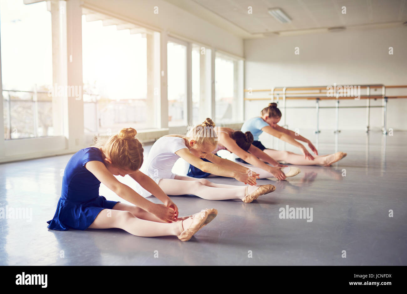 Little Ballerina ragazze flessioni e allungamenti mentre è seduto sul pavimento nella classe di balletto. Foto Stock