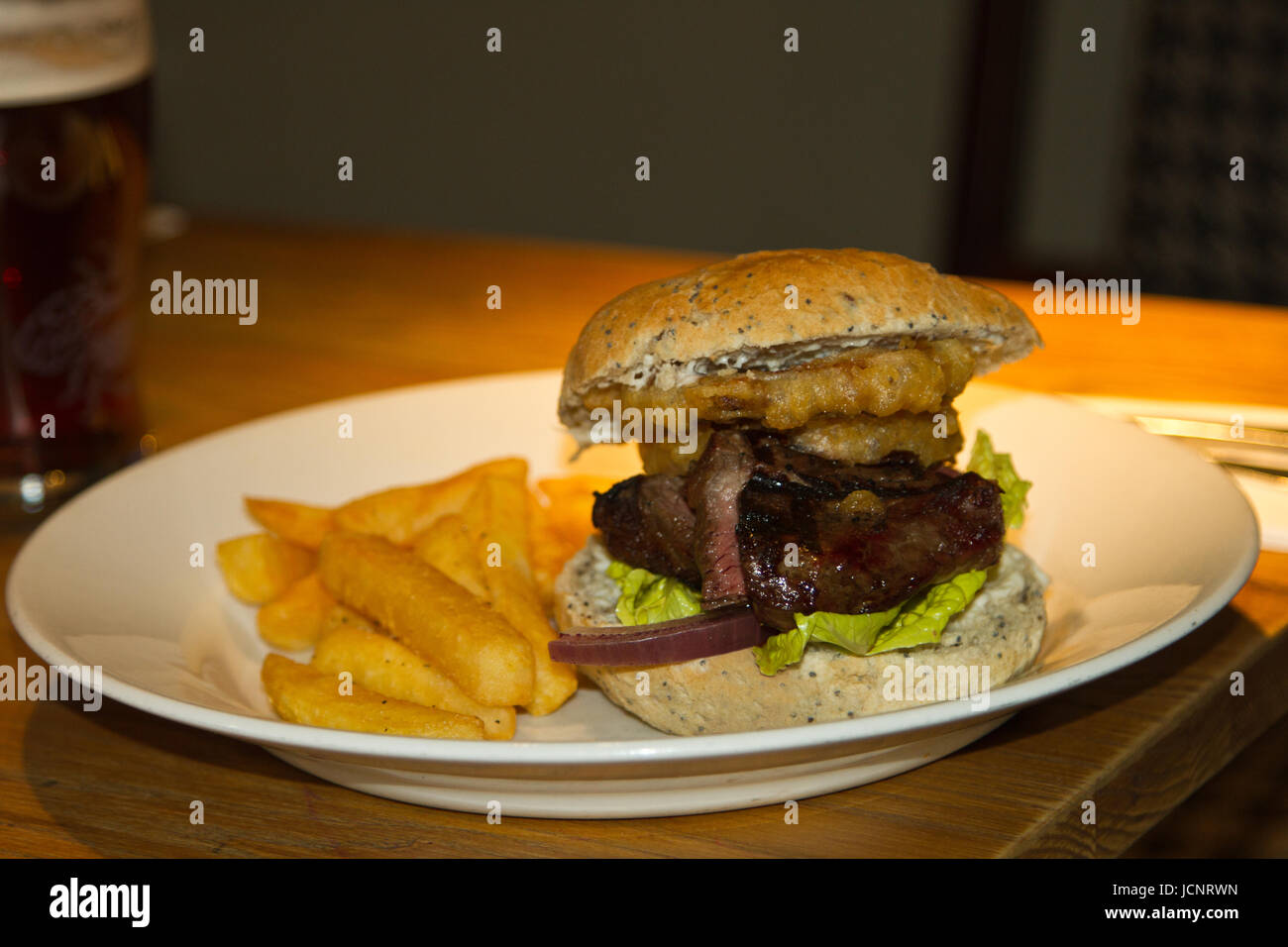 Bistecca tradizionale hamburger, patatine, anelli di cipolla con una pinta di birra generico o amaro in background. Foto Stock