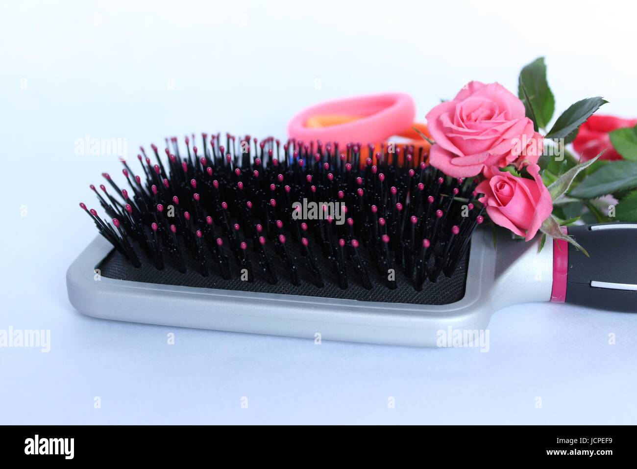 Una spazzola per capelli con rosa rosa decorativi ed elastico su sfondo bianco Foto Stock
