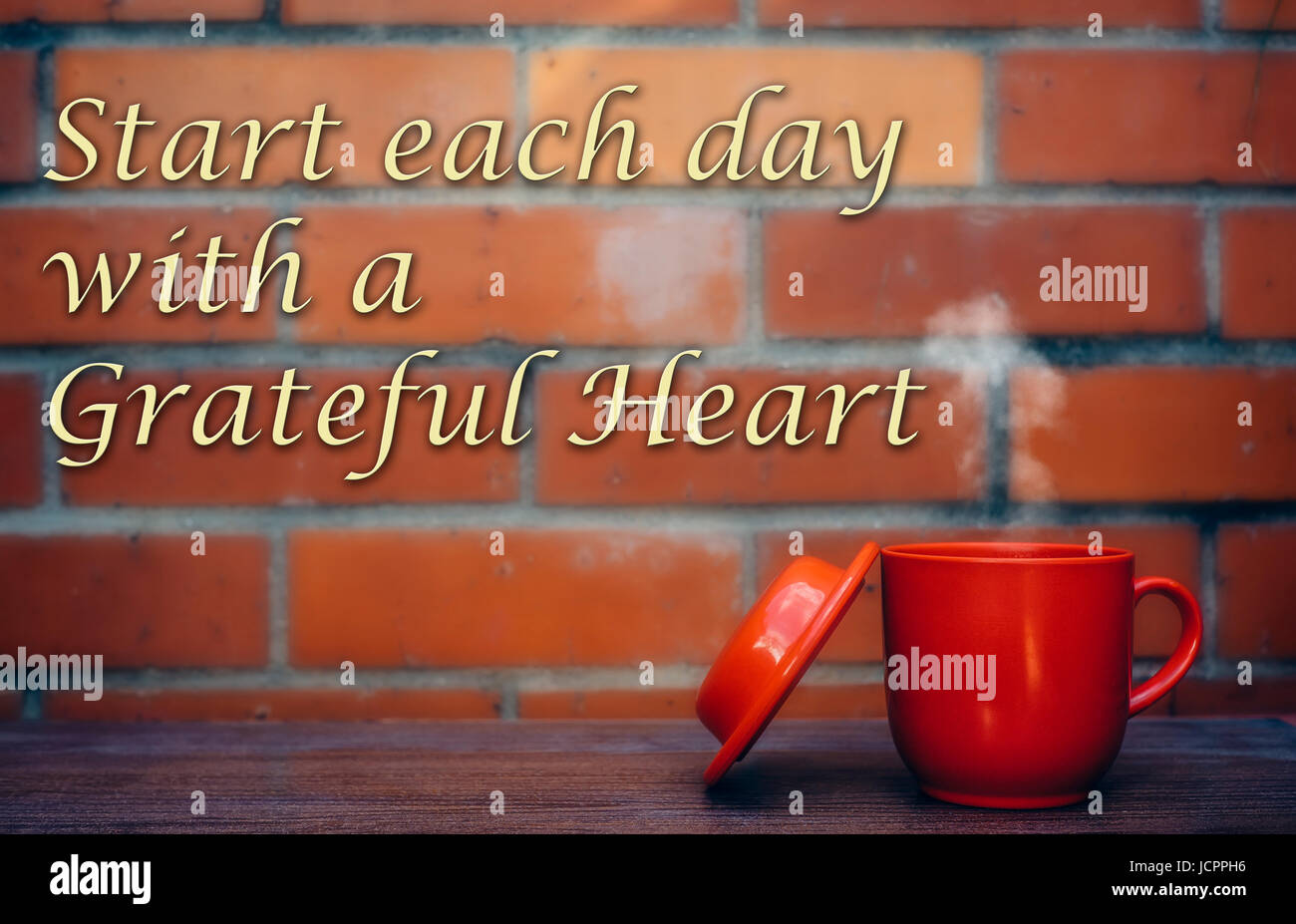 Citazioni motivazionali ' iniziare ogni giornata con un cuore grato ' con una tazza di caffè e il rosso un muro di mattoni come sfondo Foto Stock
