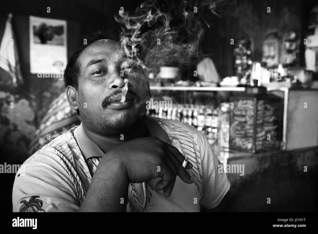 Bianco e nero ritratti immagine di un uomo indonesiano di fumare in un ristorante locale senza una cura nel mondo! Street photography al suo meglio. Foto Stock