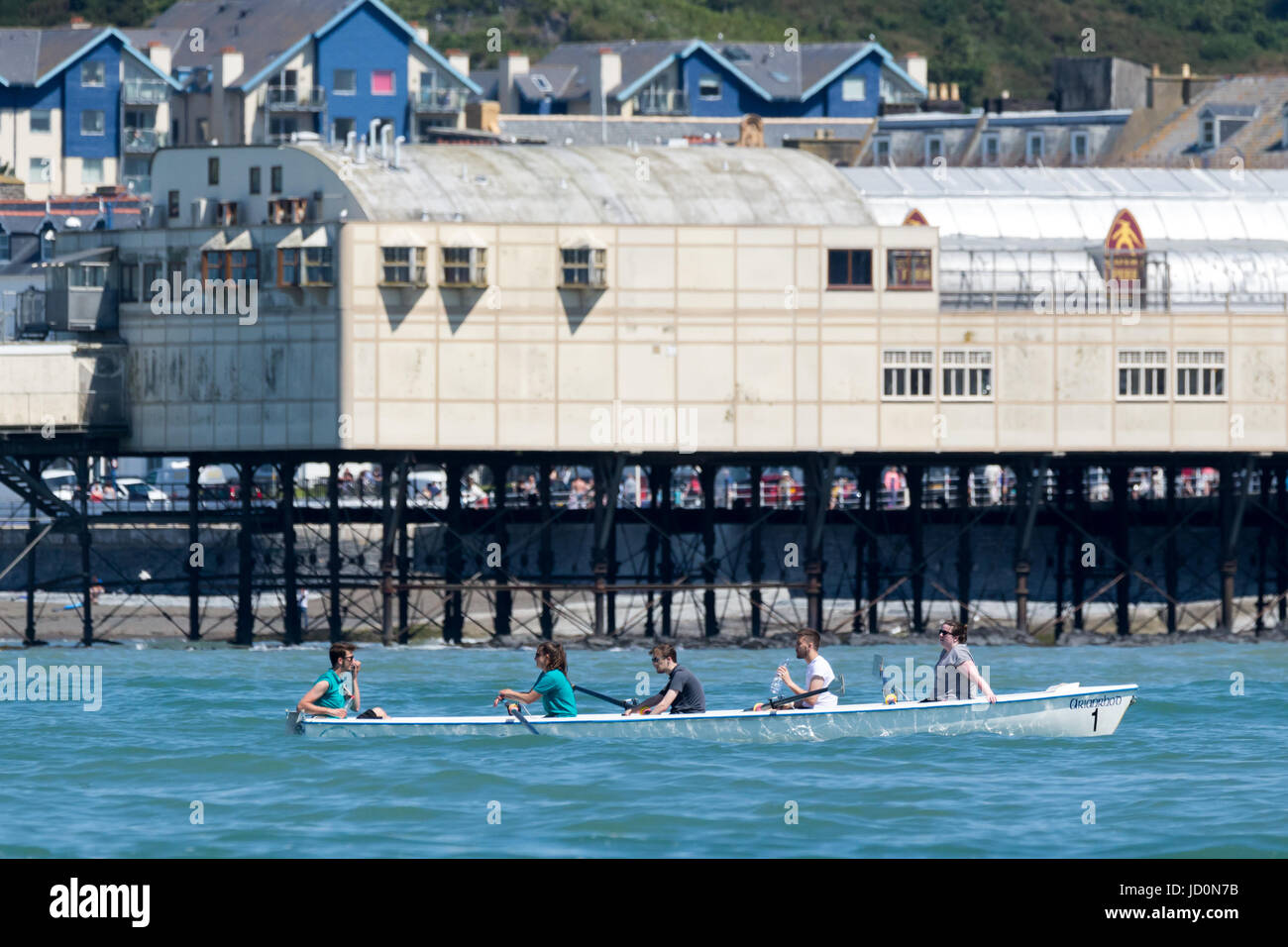 La gente in una barca a remi oltrepassando Aberystwyth pier Foto Stock