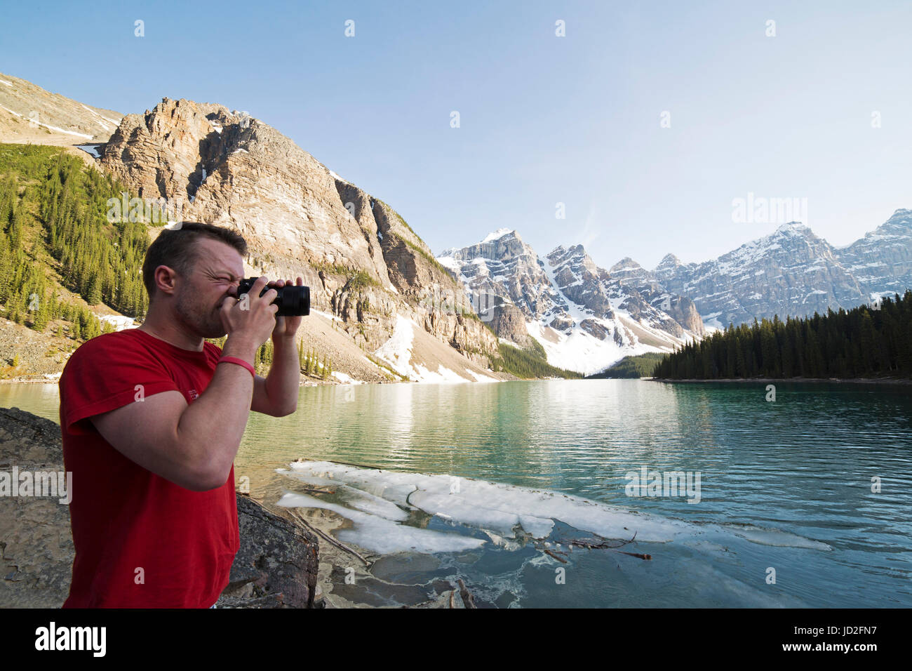 Un uomo fotografie dal Lago Moraine nelle Montagne Rocciose Canadesi a Banff National Park in Alberta, Canada. Egli indossa una T-shirt rossa. Foto Stock