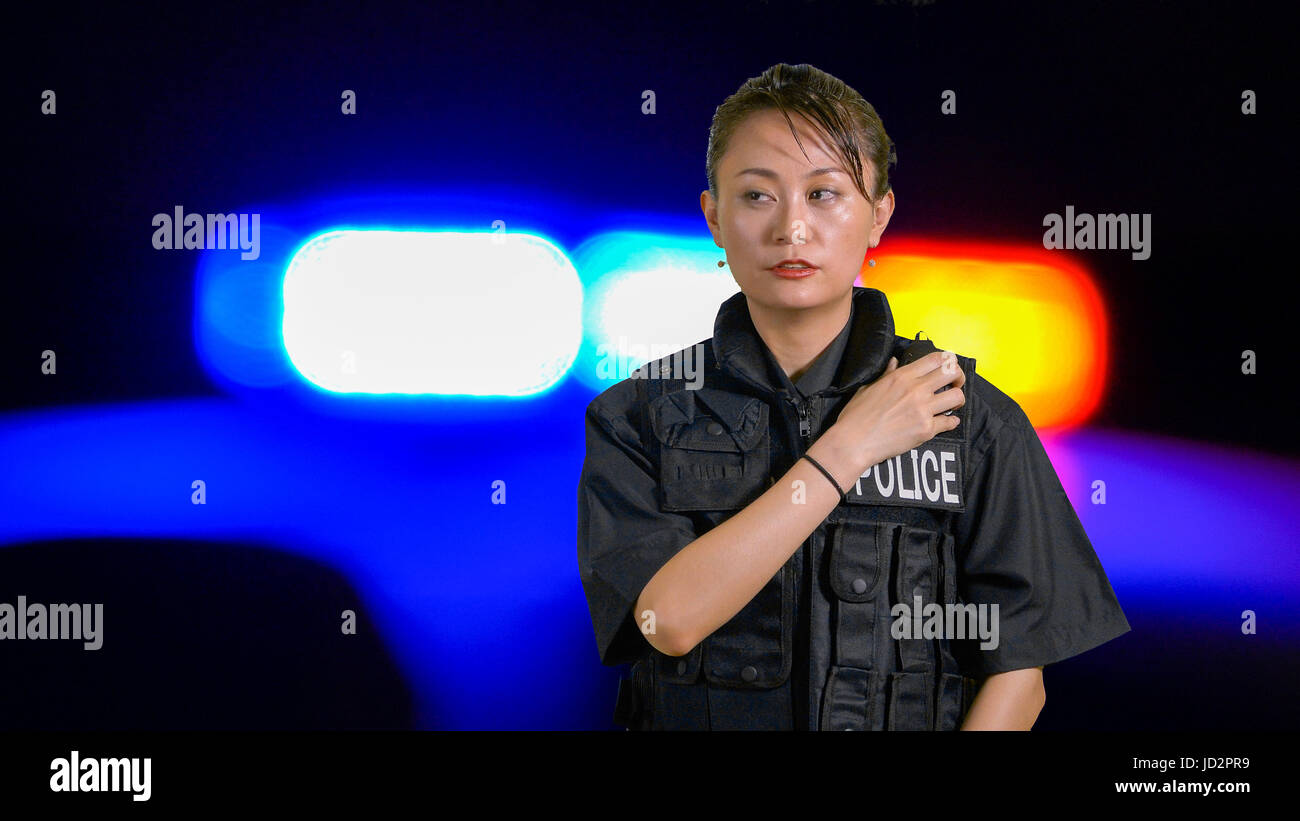 Americano asiatico poliziotta utilizzando radio della polizia con sirena e nastro di confine in background Foto Stock