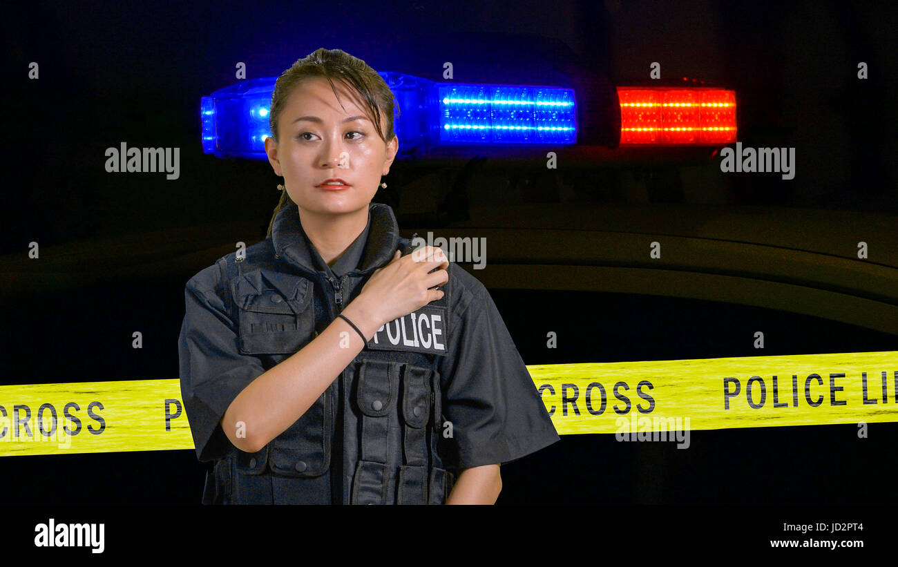 Americano asiatico poliziotta utilizzando radio della polizia con sirena e nastro di confine in background Foto Stock