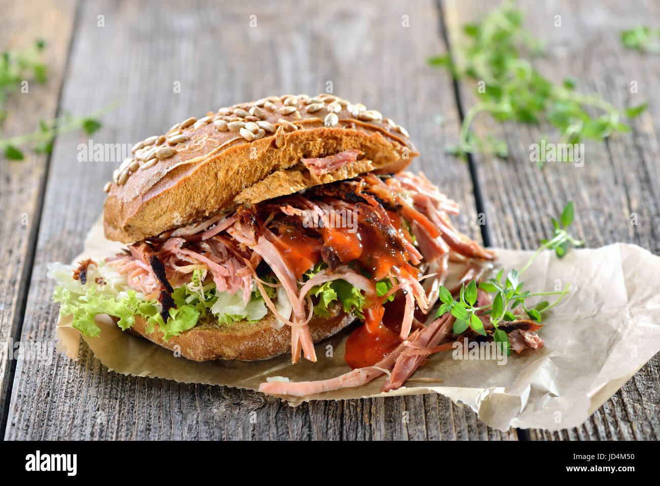 Cucina di strada: barbecue di carne di maiale tirato sandwich integrale con coleslaw, hot BBQ SAUCE servita su carta da imballaggio marrone su un sfondo di legno Foto Stock
