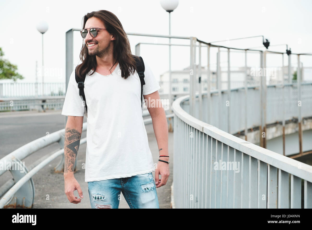 Tanga elegante modello con capelli lunghi stile di vita in strada. Vestito con una T-shirt bianco e strappato jeans blu nella città Foto Stock