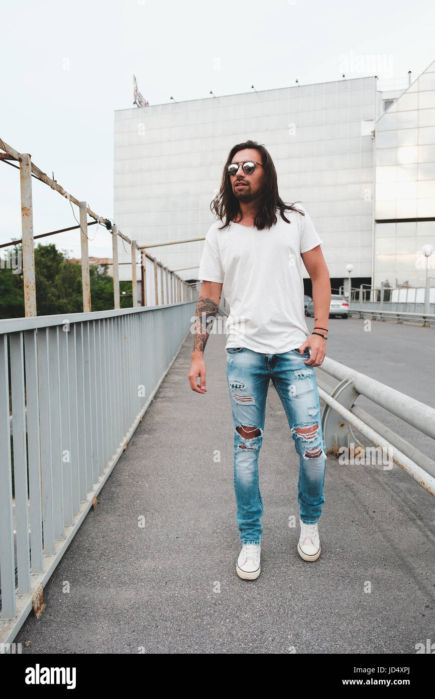 Tanga elegante modello con capelli lunghi stile di vita in strada. Vestito con una T-shirt bianco e strappato jeans blu nella città Foto Stock