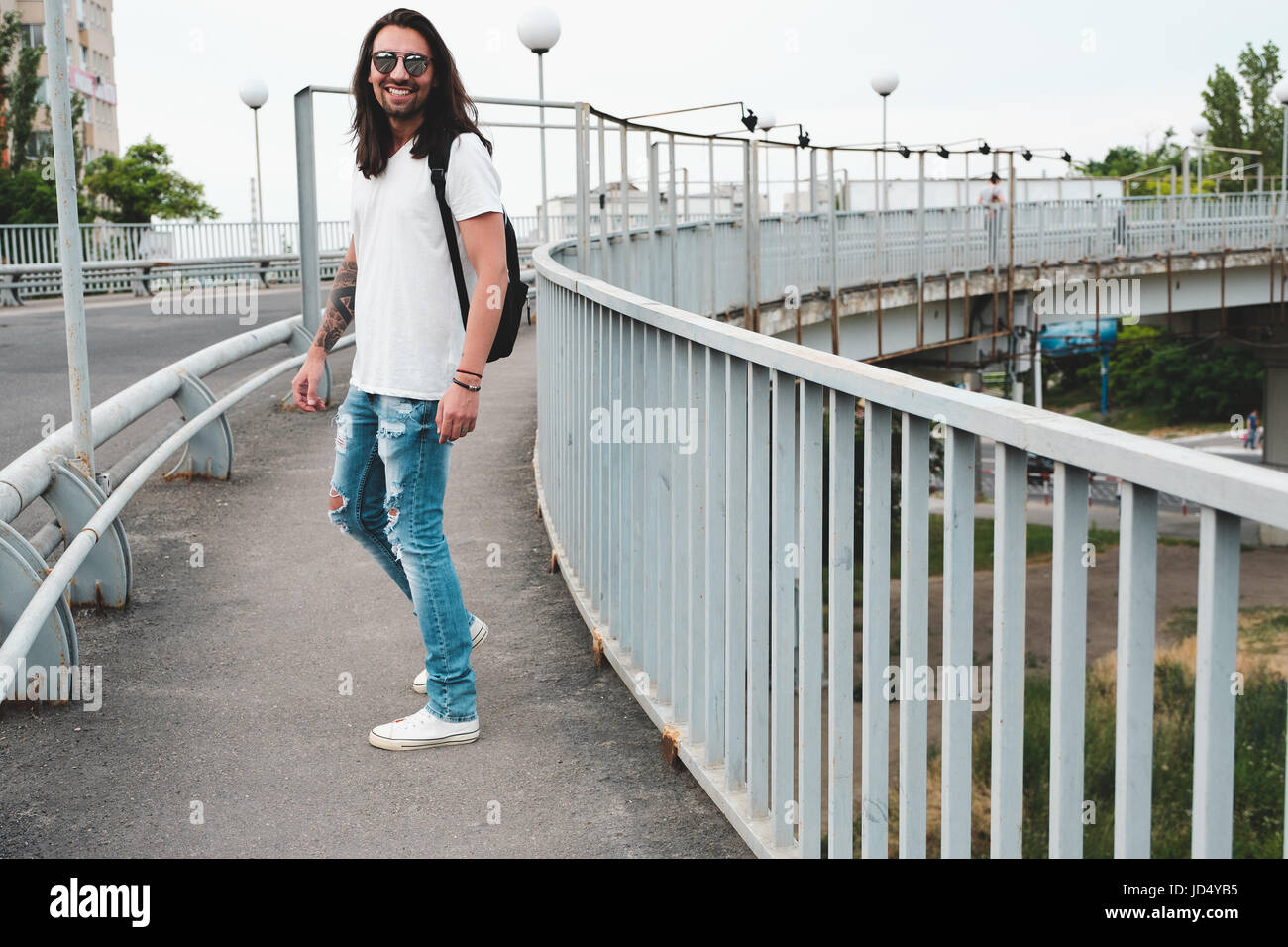 Tanga elegante modello con capelli lunghi stile di vita in strada. Vestito con una T-shirt bianco e strappato jeans blu nella città Foto Stock