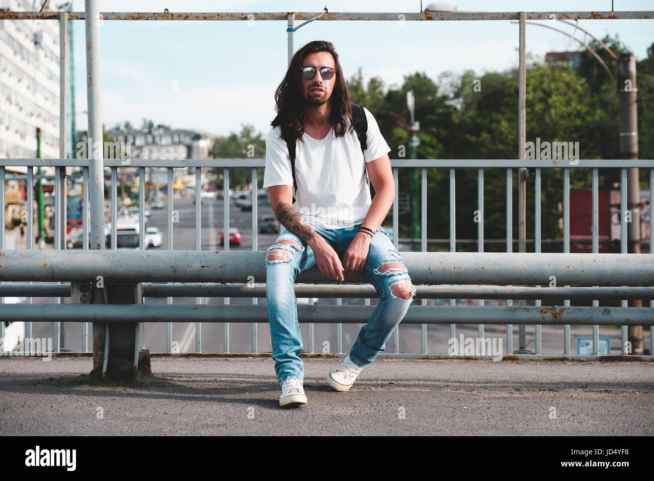 Tanga elegante modello con capelli lunghi stile di vita in strada. Vestito con una T-shirt bianco e strappato jeans blu nella città Foto Stock