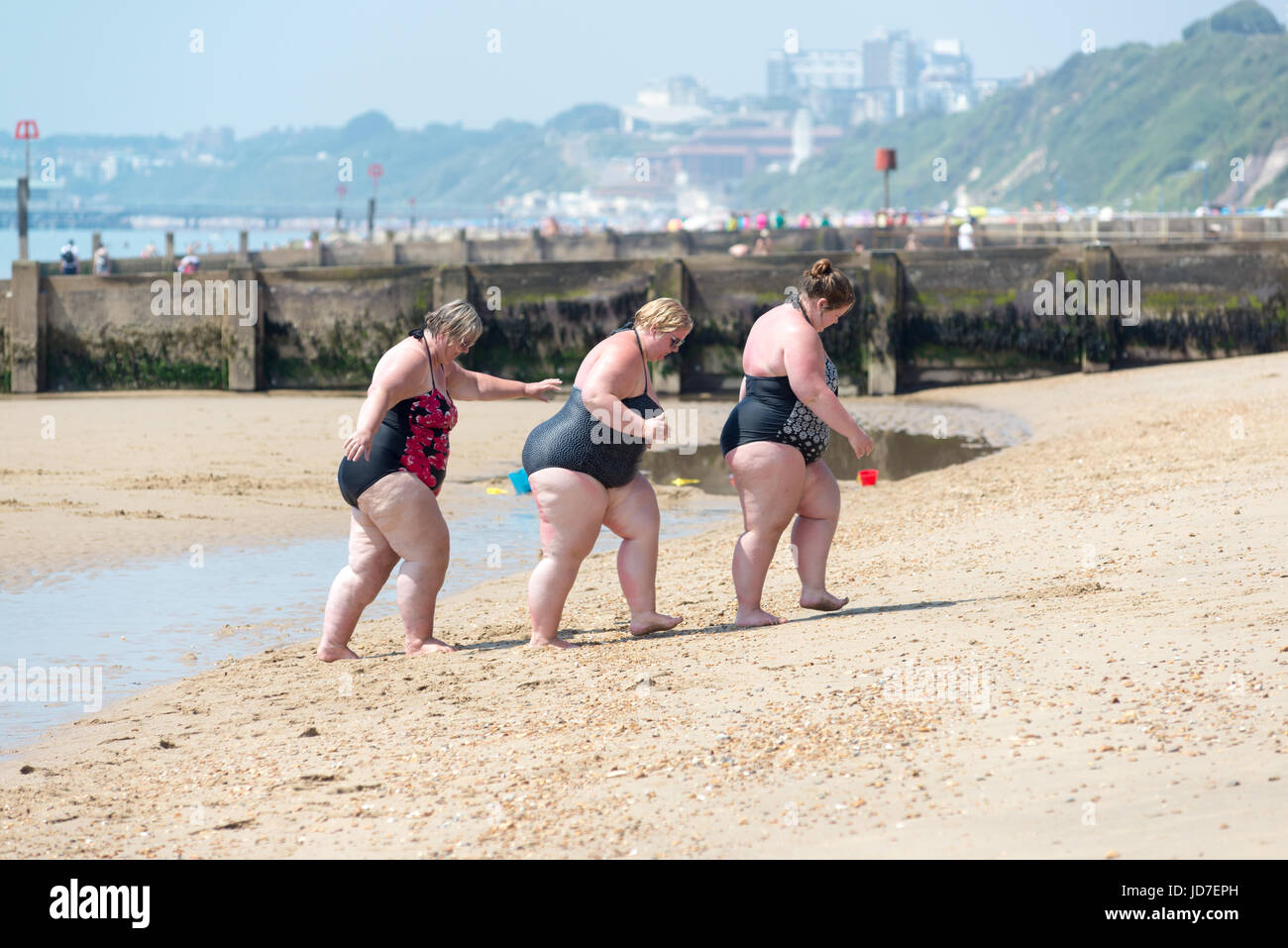Tre donne in sovrappeso che indossano costumi da bagno che camminano su una spiaggia di mare inglese in estate. Foto Stock
