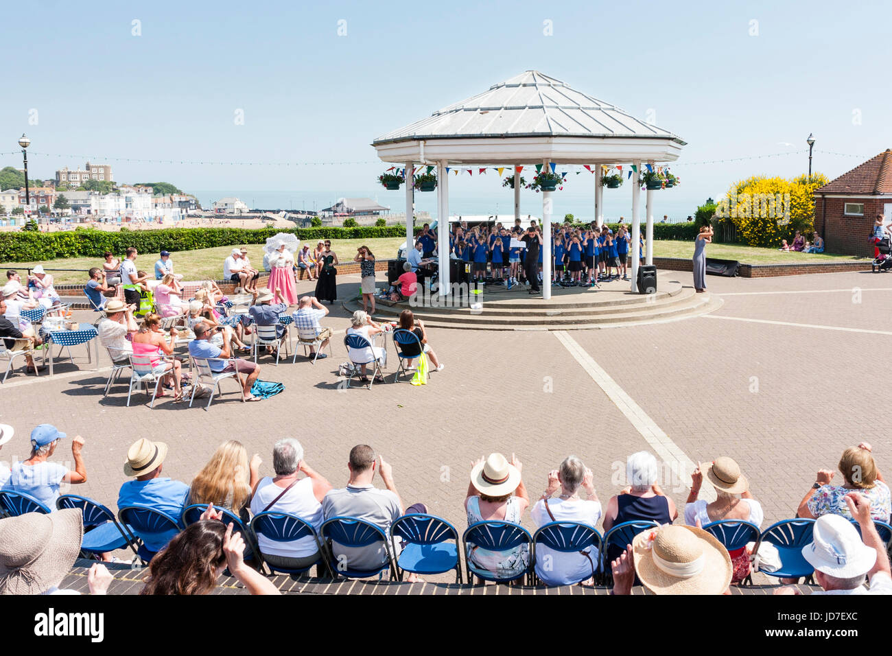 I bambini della scuola elementare, 9-10 anni, coro, tutti vestiti in blu, in piedi sul cavalletto di banda in estate tempo eseguendo concerto all'aperto con il pubblico a guardare. Upton coro scolastico durante il Broadstairs Dickens settimana. Foto Stock