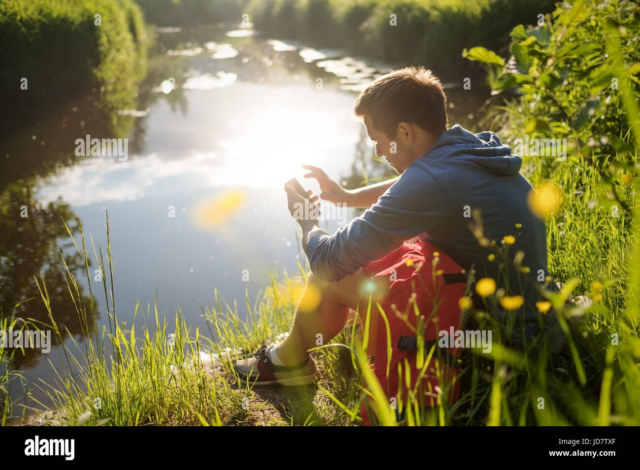 Giovane uomo seduto accanto al fiume con caffè e godendo in giornata soleggiata. Foto Stock