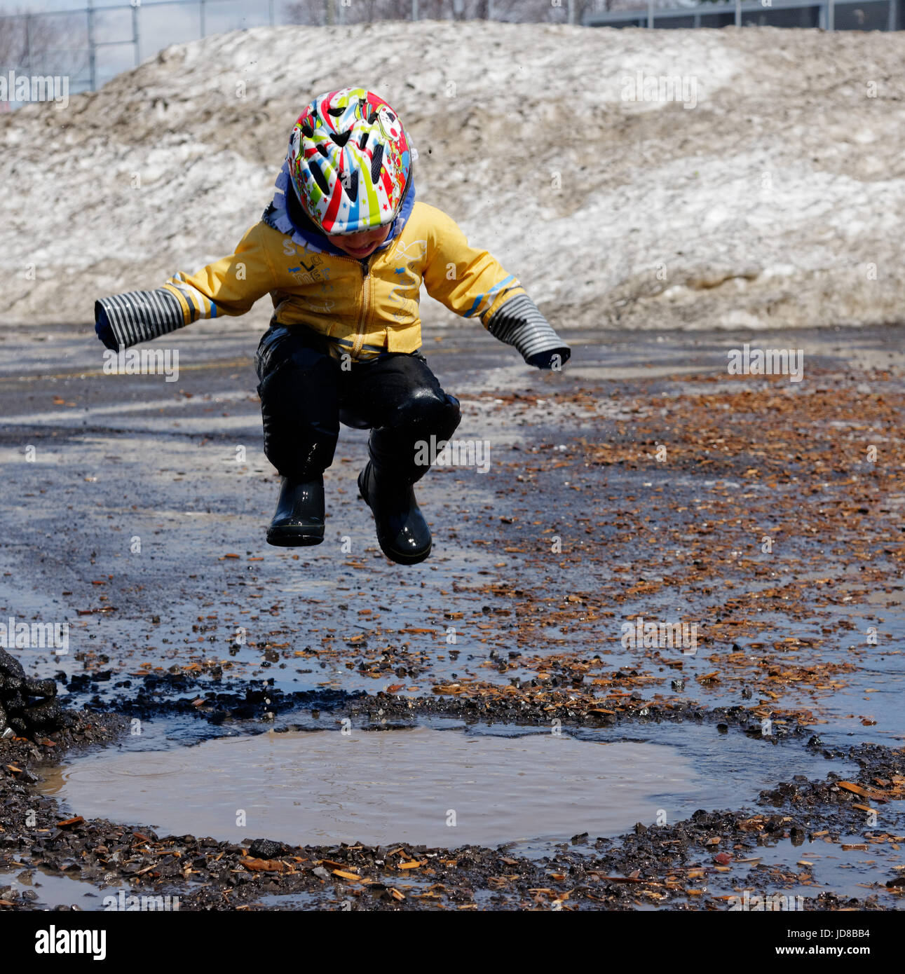 Un giovane ragazzo (5 anni) saltando in una pozza di fango. Foto Stock