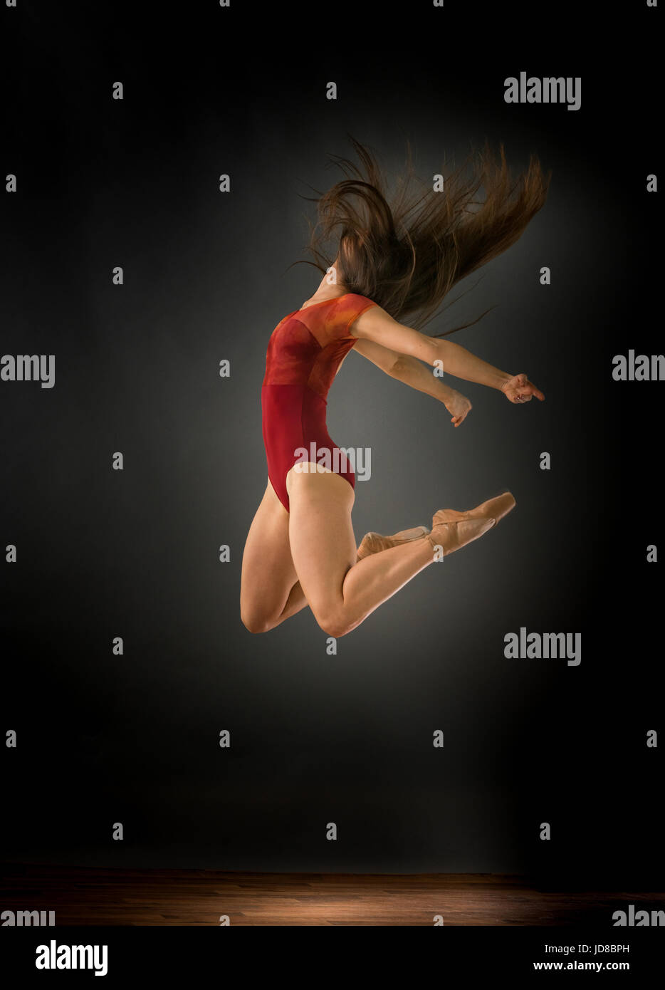 Femmina ballerina jumping metà aria, con i capelli che ricopre la faccia e braccia dietro, studio shot. caucasian montare piuttosto skinny athletic Foto Stock