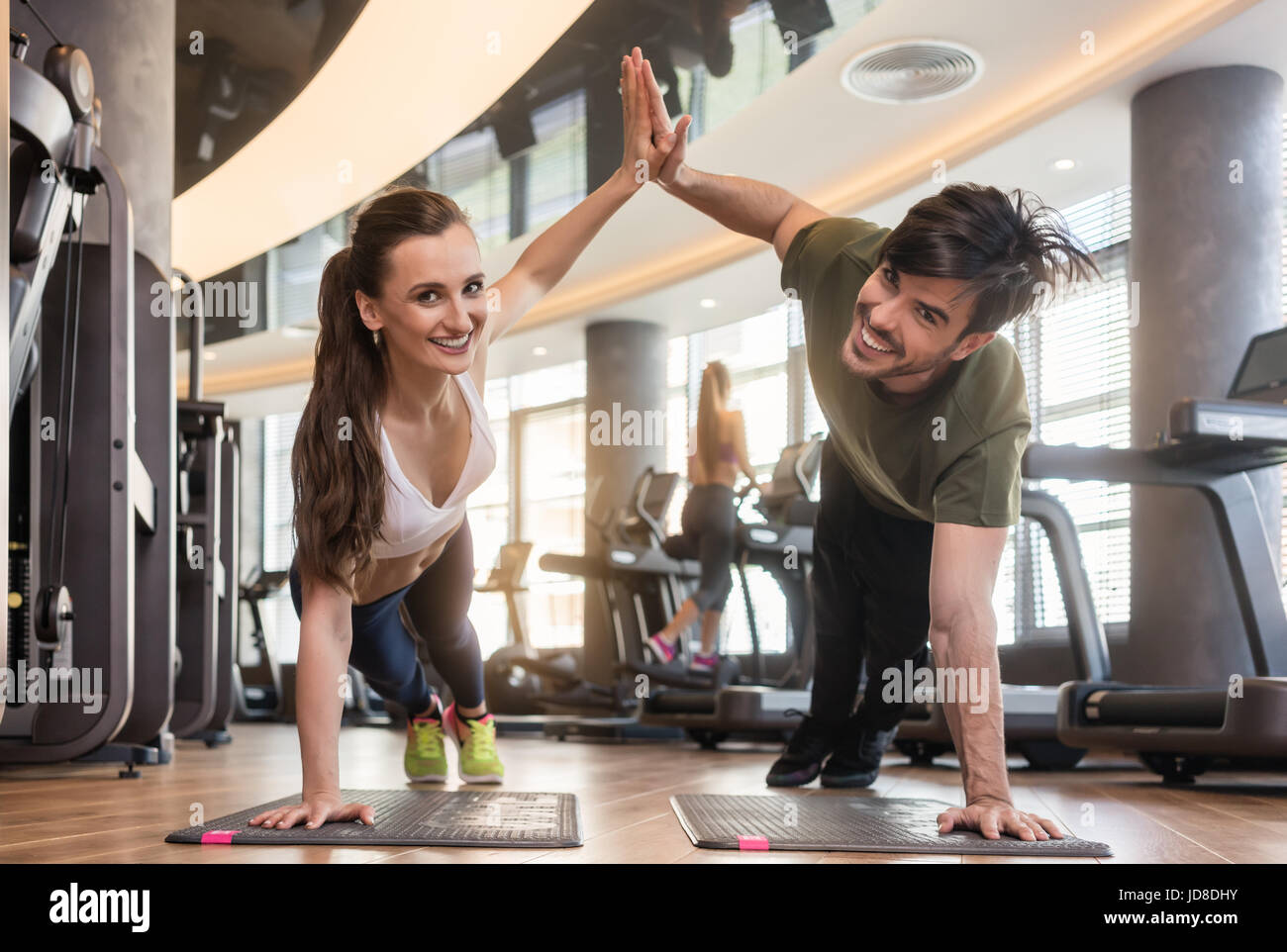 Montare giovane uomo e donna sorridente e guardando la telecamera mentre dando alta cinque dalla tavola di base pone durante gli allenamenti in palestra Foto Stock