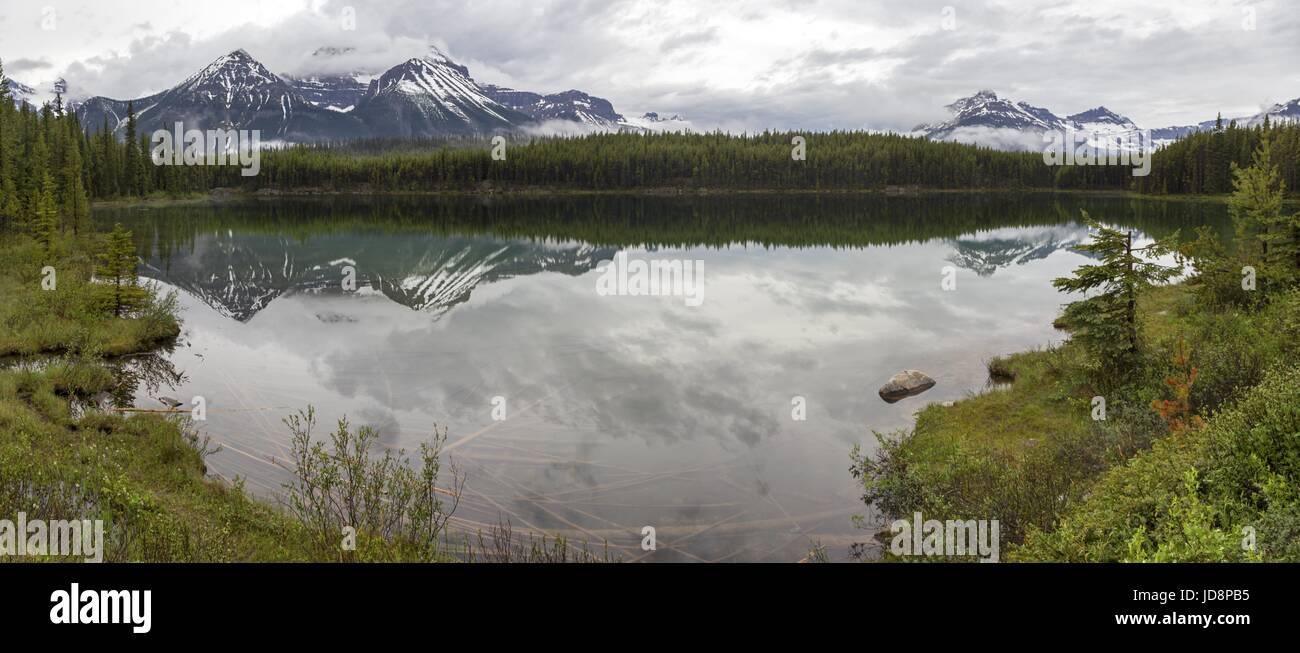 Cime innevate delle Montagne Rocciose che si riflettono nella calma acqua del lago Herbert. Paesaggio panoramico del giorno nuvoloso, Parco Nazionale di Banff, Canada Foto Stock