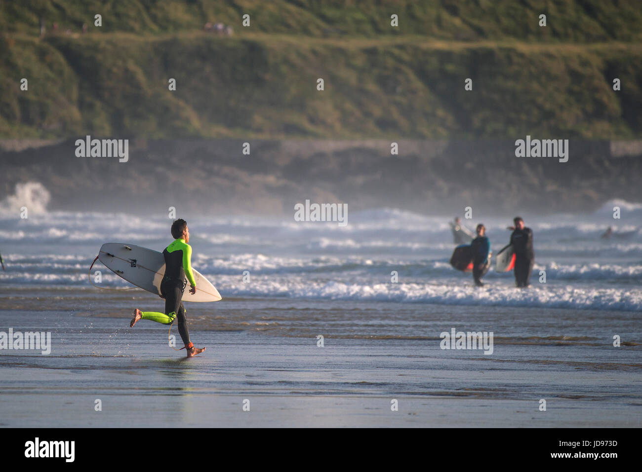 Un surfista in esecuzione nel mare a Fistral Beach in Newquay, Cornwall. Foto Stock