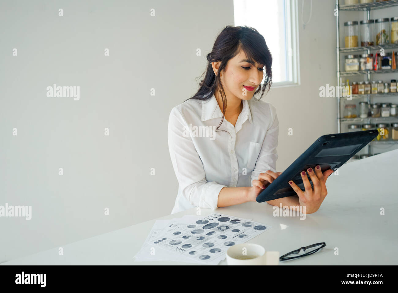 Giovane donna con tavoletta digitale interni a scrivania in cucina. i giovani adulti arabo piuttosto 20 anni Foto Stock
