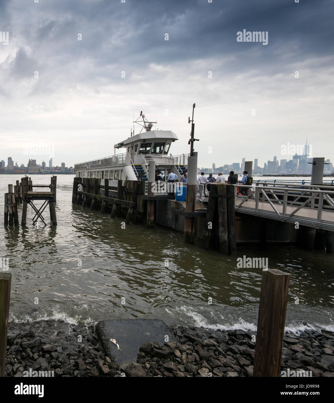 Il passeggero barca dal jetty di legno di inguine in primo piano e ciottoli a riva, New York, Stati Uniti d'America. 2016 città urbana negli Stati Uniti d'America Foto Stock