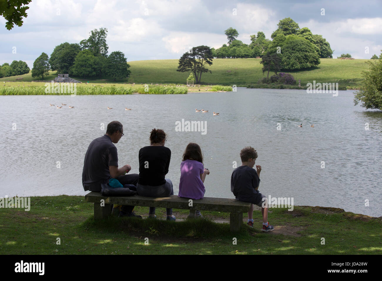 Famiglia seduto in riva al lago a Arundel giardini paesaggistici, Arundel Castle, West Sussex, in Inghilterra, Regno Unito Foto Stock