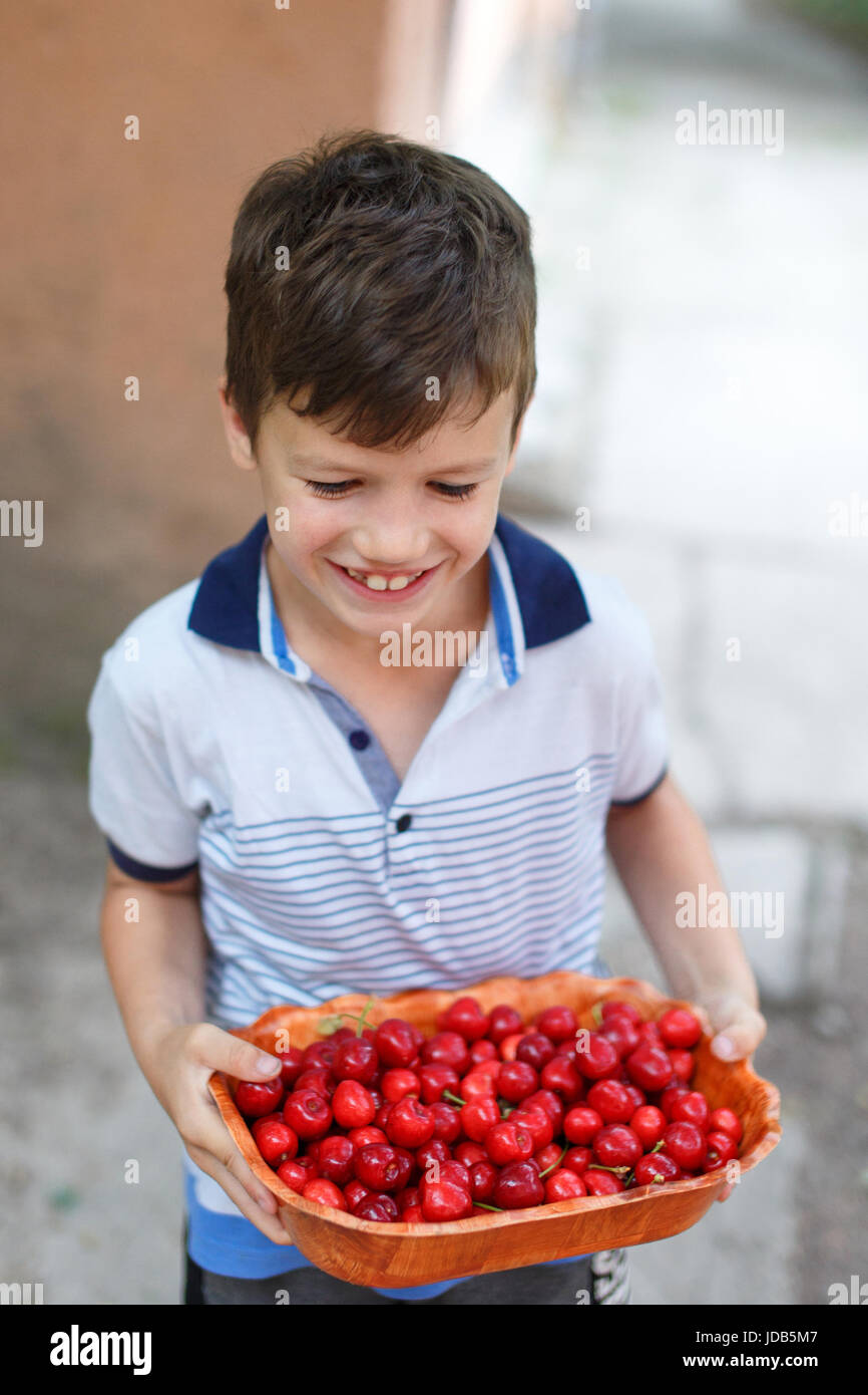 Piccolo felice smiley kid tenendo le ciliegie di ciotola Foto Stock