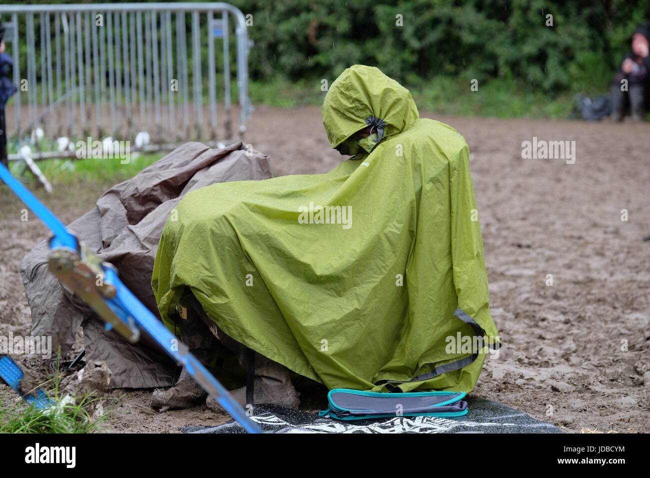 Festival goer seduto in una pioggia poncho e wellies in un fangoso festival di musica Foto Stock