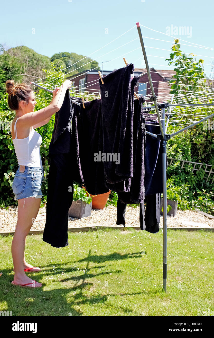 Giovane donna nel suo 20s appendere fuori il lavaggio a secco nel giardino sul retro in una calda giornata estiva REGNO UNITO Foto Stock