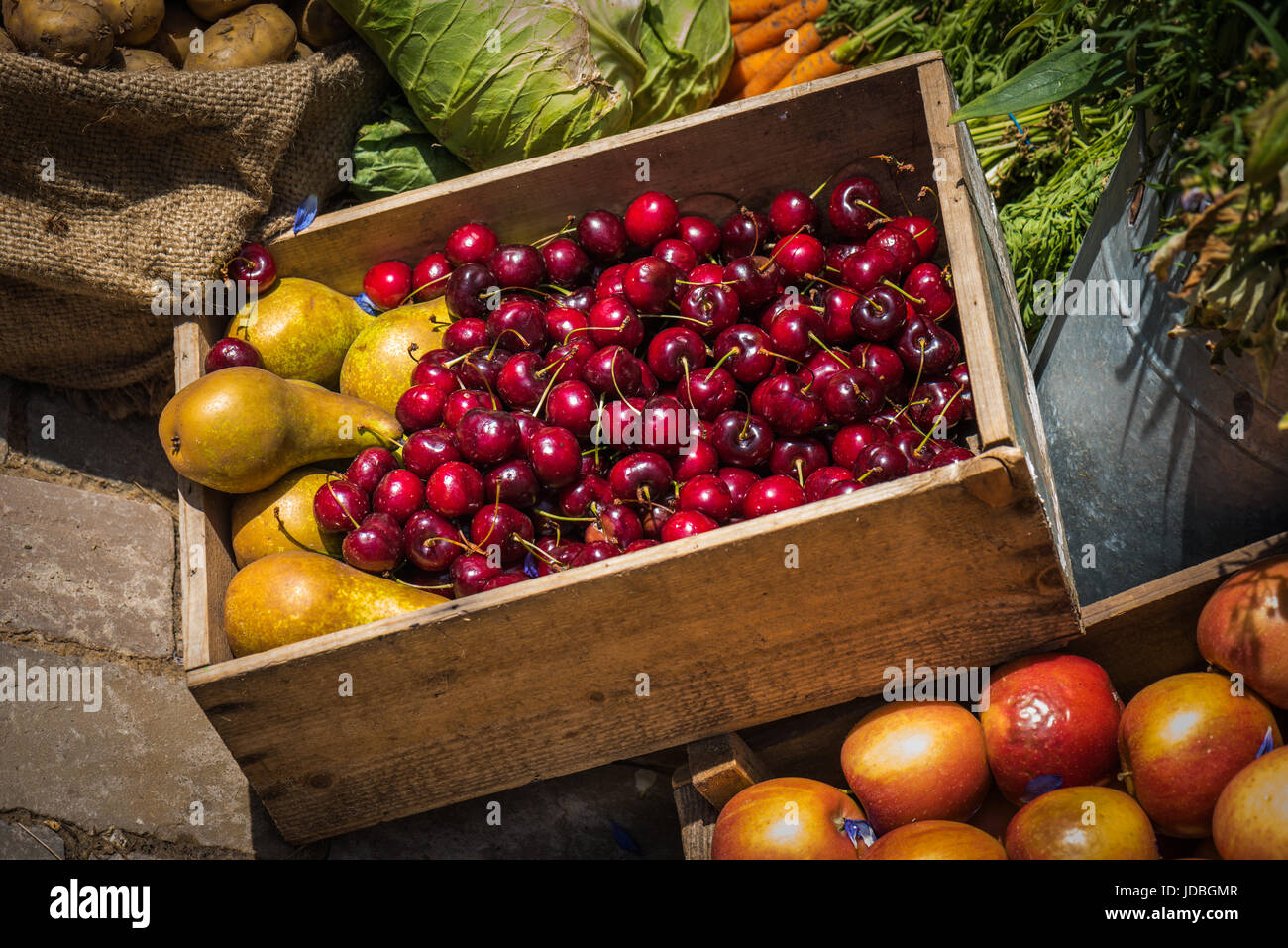 Una casella di visualizzazione di ciliegie e pere circondato da diversi tipi di frutta e verdura Foto Stock