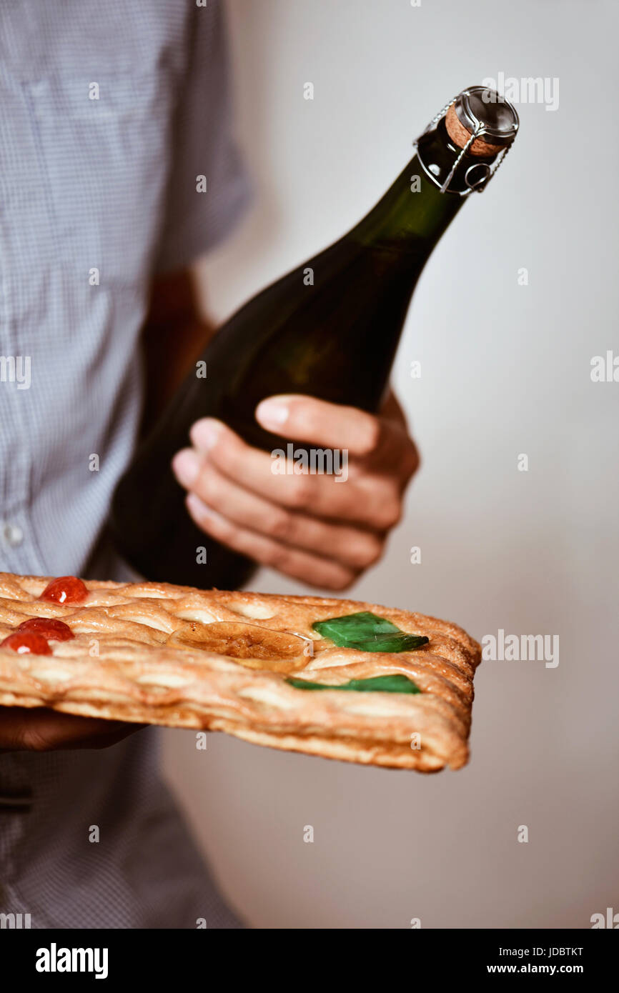 Primo piano di un giovane uomo caucasico con una bottiglia di champagne e una coca de Sant Joan, un tipico dolce torta piatta dalla Catalogna, Spagna, mangiato su Saint J Foto Stock