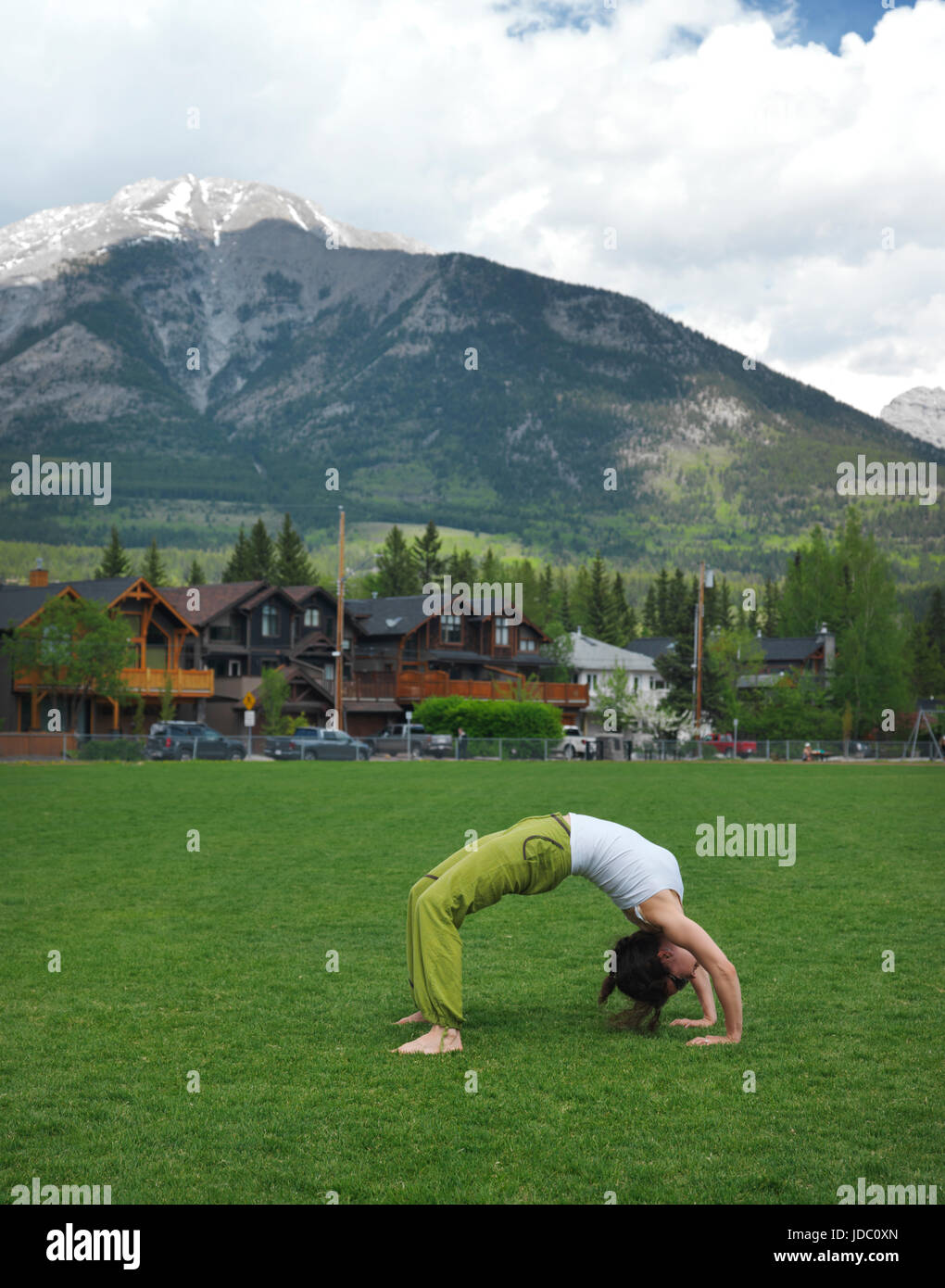Giovane donna a praticare yoga, ponte facendo esercizio all'aperto in Centennial Park in Canmore, città in Alberta's Rockies con montagne rocciose in backg Foto Stock