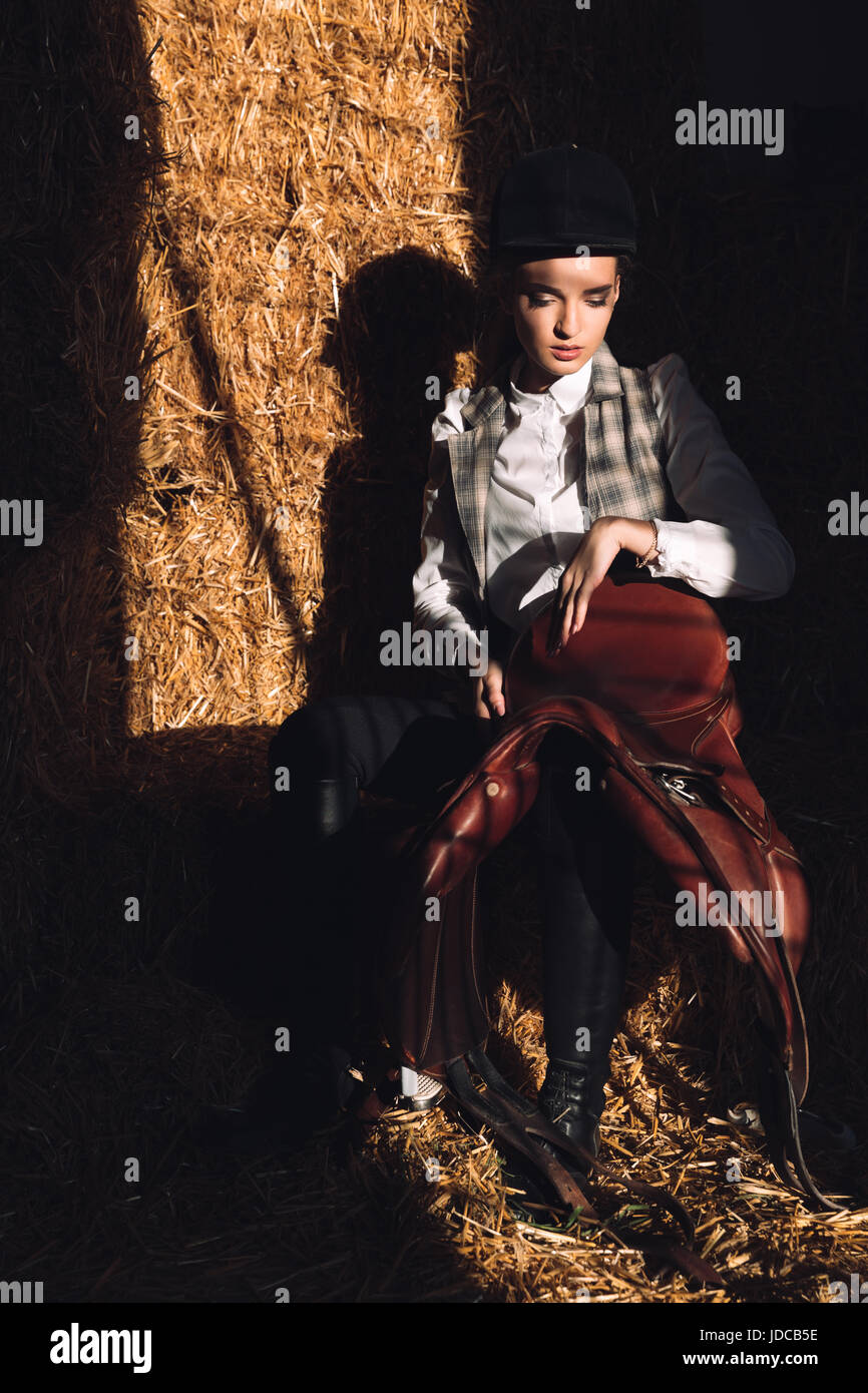 Immagine di grave giovane ragazza seduta nel fienile con seddle. Guardando a parte Foto Stock