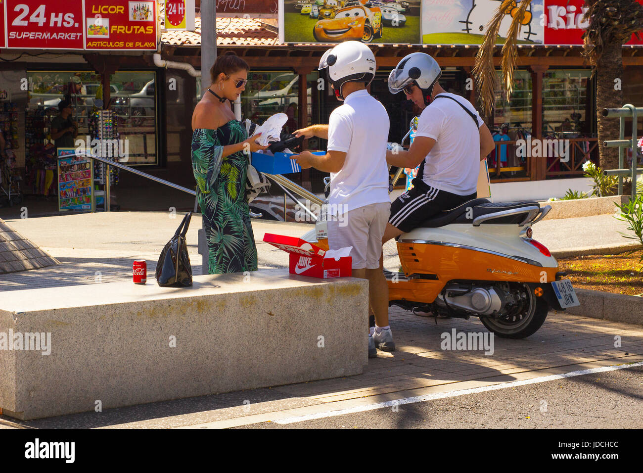 Un affascinante signora giovane a chiacchierare con due maschi motociclisti sulla strada principale di Playa Las Americas in Teneriffe Foto Stock
