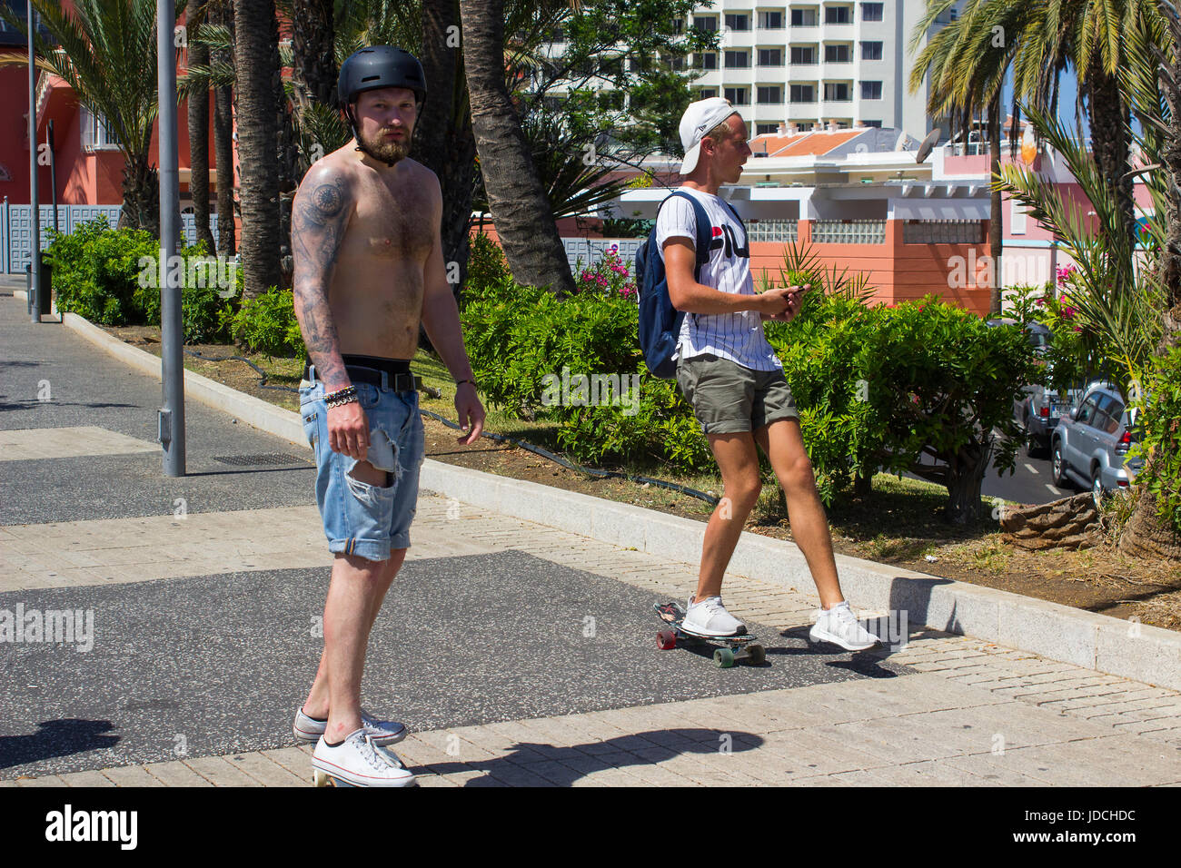 Due maschio skateboarders colto di sorpresa come essi crociera lungo la via principale di Playa Las Americas in Teneriffe Foto Stock